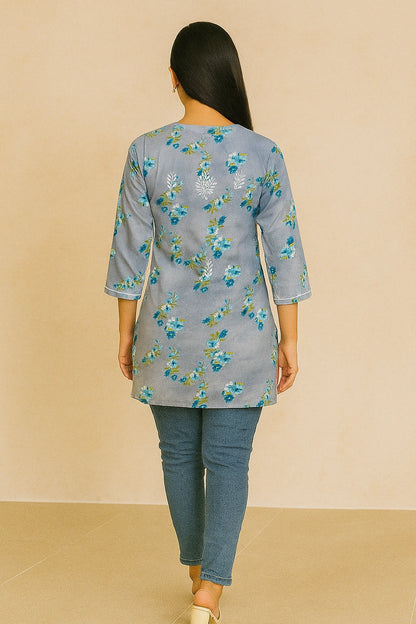 Woman wearing a lucknowi chikankari grey top with white polka dots and blue jeans on a gray background