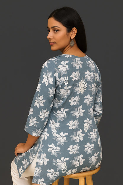 Woman wearing a lucknowi chikankari grey top with white polka dots and blue jeans on a gray background