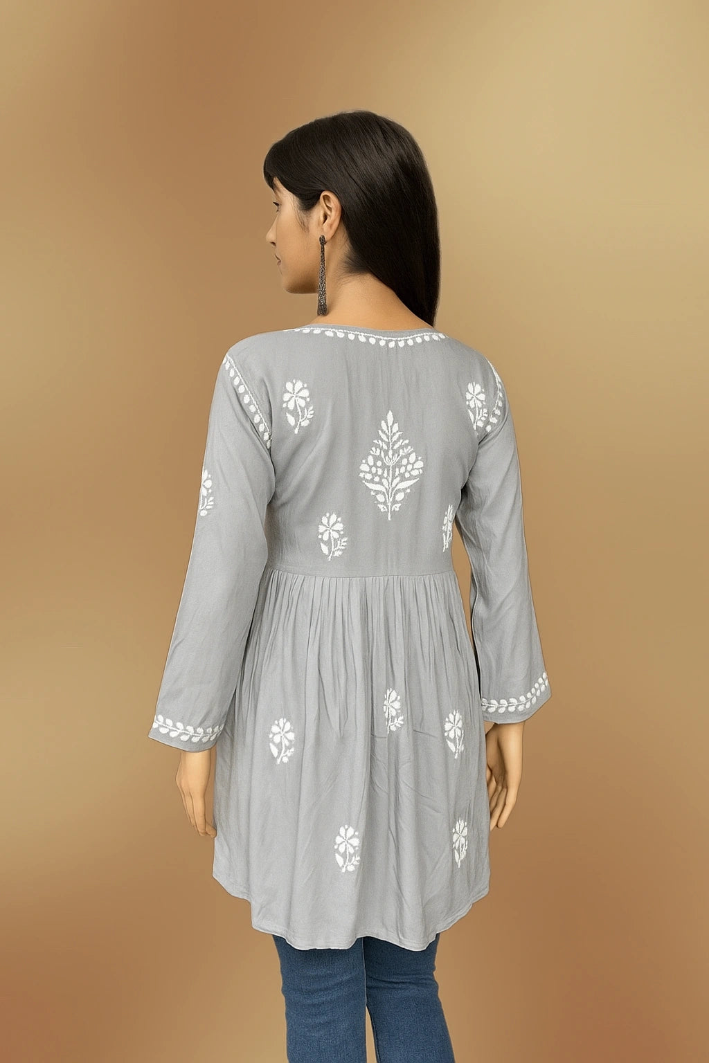 Woman wearing a lucknowi chikankari grey top with white polka dots and blue jeans on a gray background