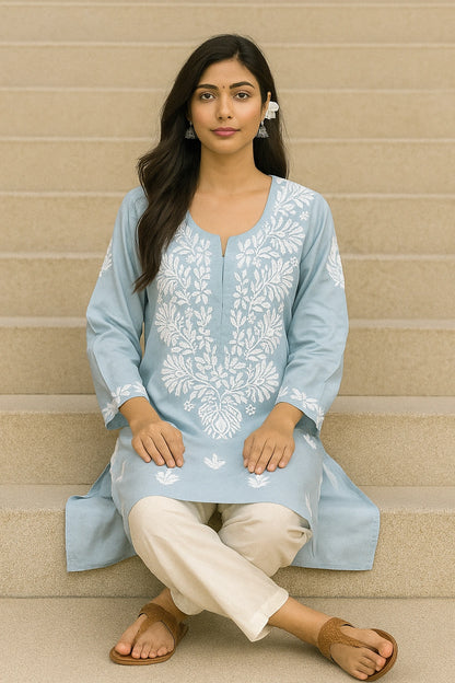 Woman wearing a light blue embroidered kurta with white pants against a beige wall.