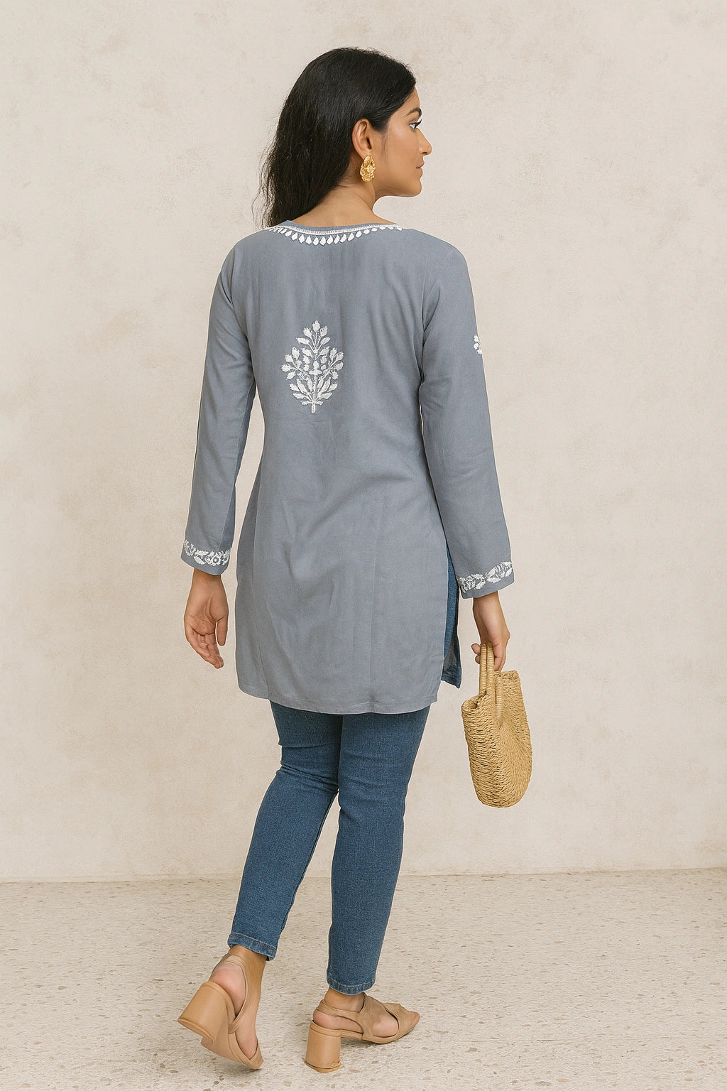 Woman wearing a lucknowi chikankari grey top with white polka dots and blue jeans on a gray background