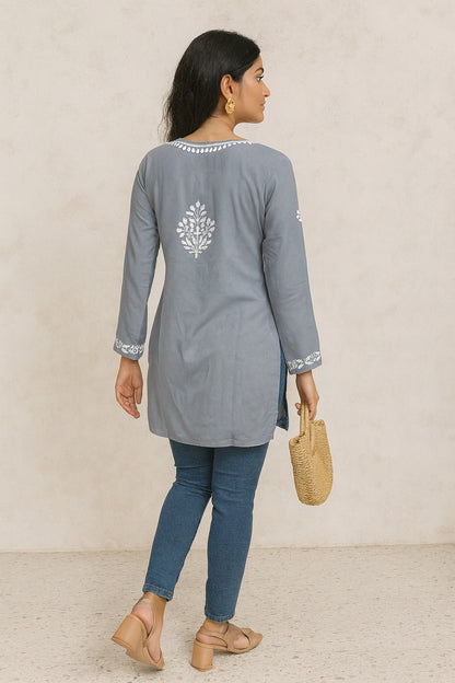 Woman wearing a lucknowi chikankari grey top with white polka dots and blue jeans on a gray background