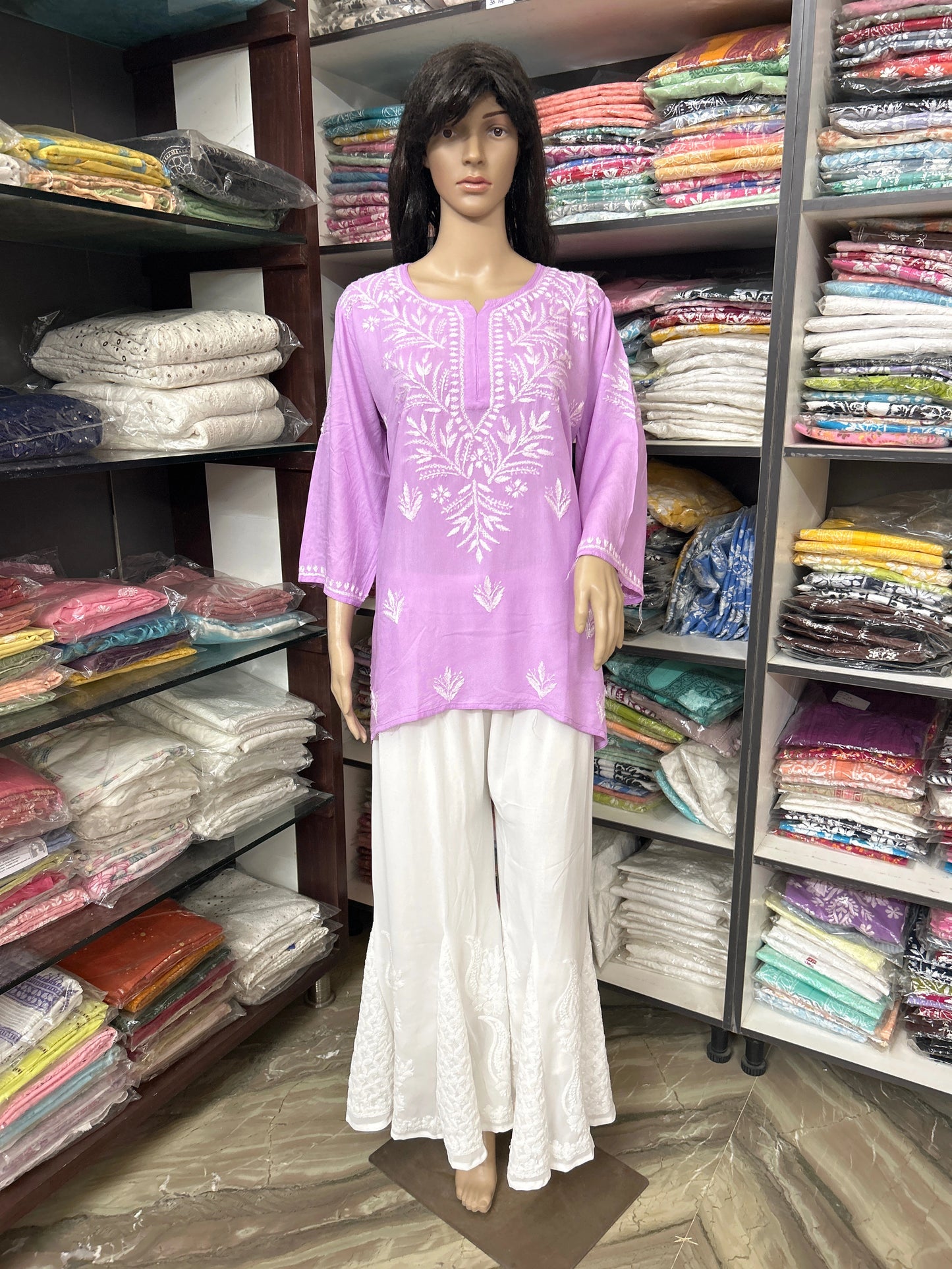 Mannequin wearing a purple embroidered top and white pants in a fabric store.