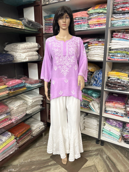 Mannequin wearing a purple embroidered top and white pants in a fabric store.