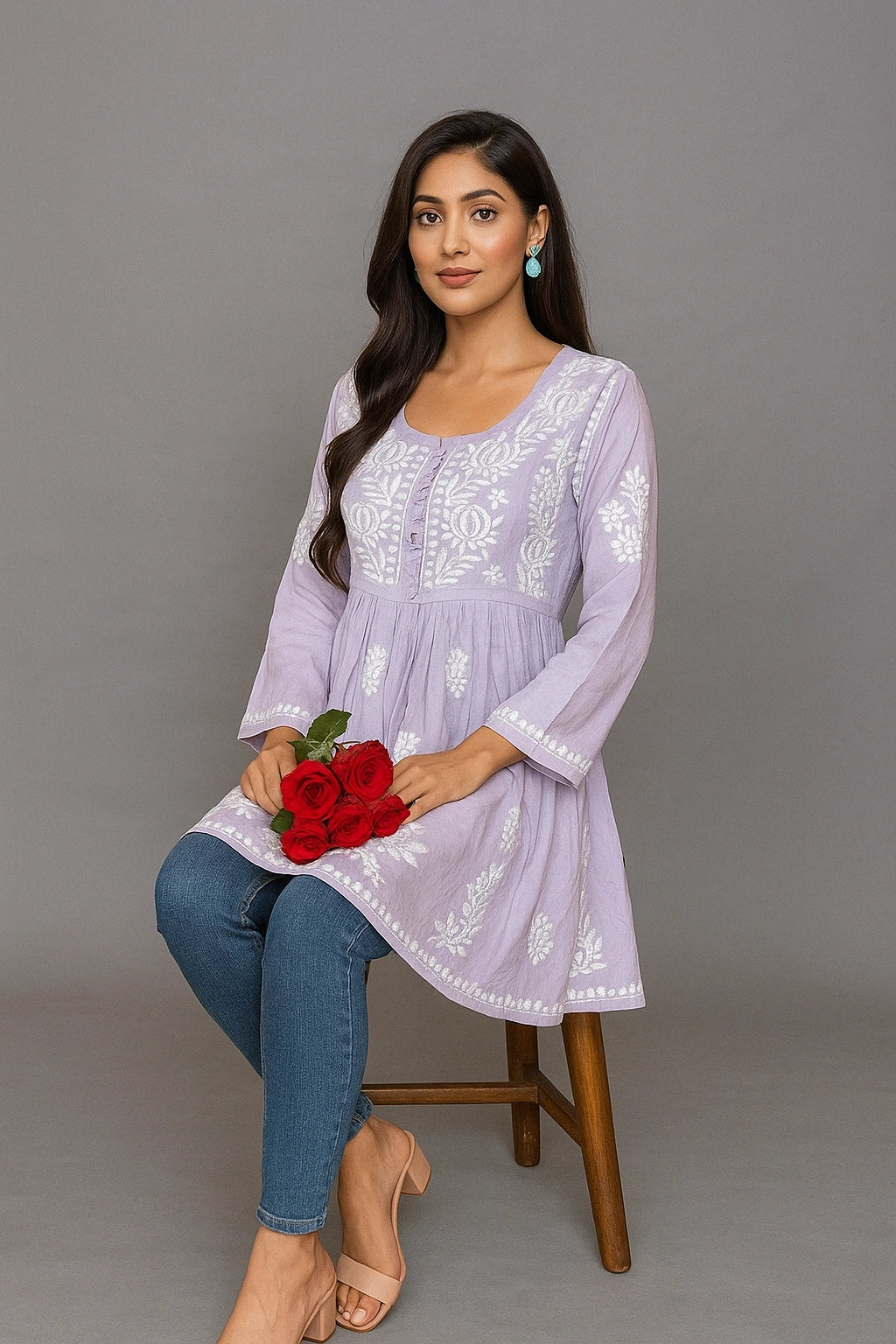 Woman in a light purple embroidered dress holding red flowers against a gray background