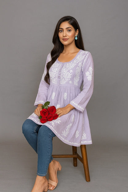 Woman in a light purple embroidered dress holding red flowers against a gray background