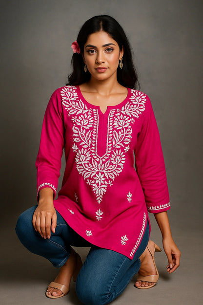 Woman wearing a pink embroidered top and blue jeans on a gray background