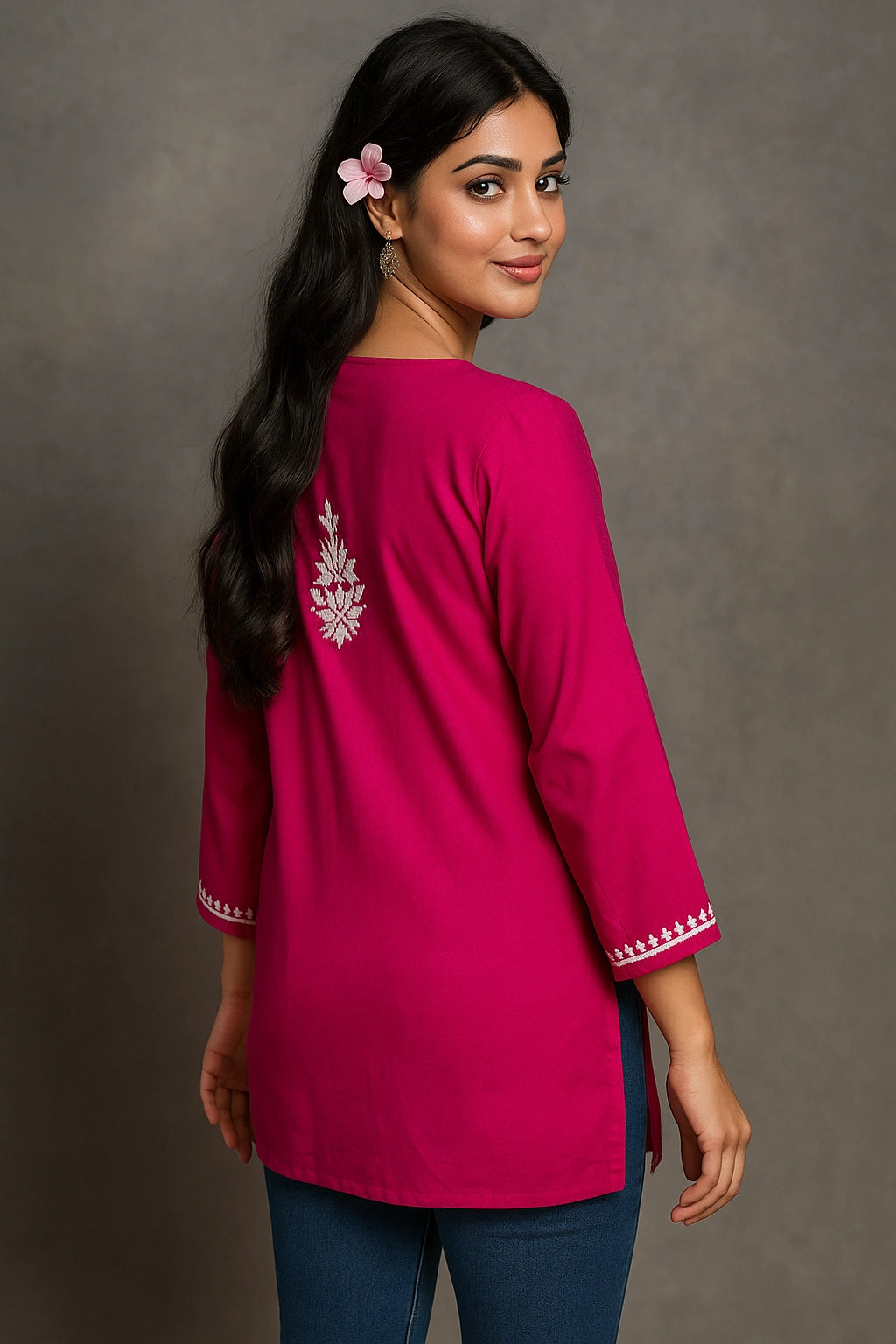 Woman wearing a pink embroidered top against a gray background