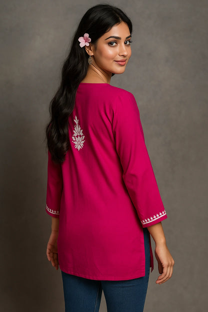 Woman wearing a pink embroidered top against a gray background