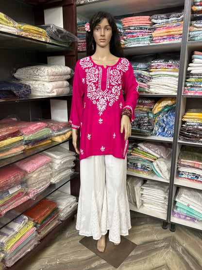 Mannequin wearing a pink embroidered top and white pants in a fabric store.