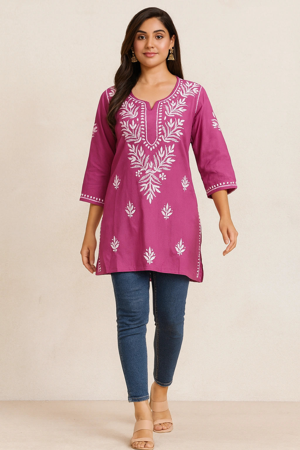 Woman wearing a purple embroidered tunic with blue jeans on a beige background