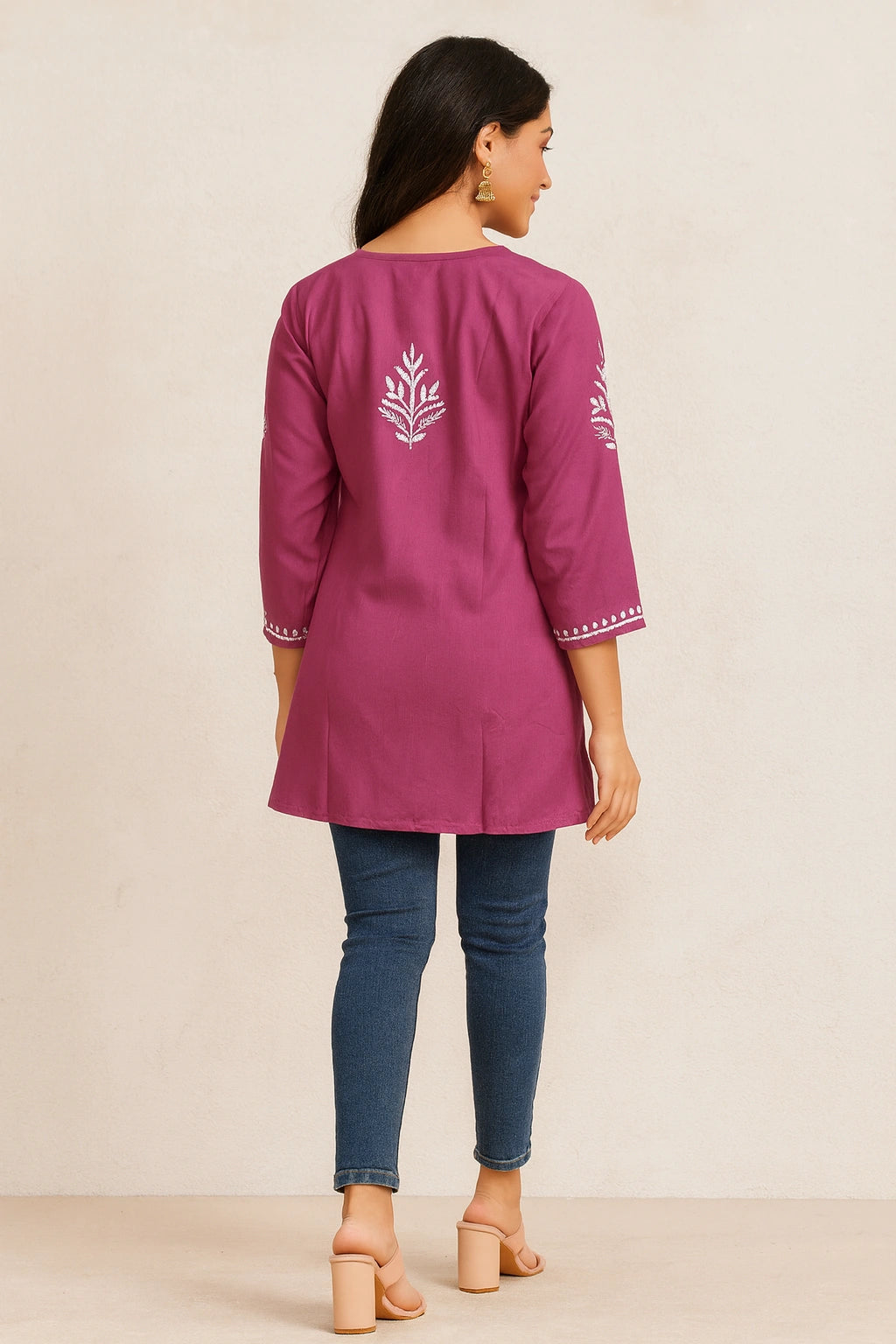 Woman wearing a magenta embroidered kurta with blue jeans on a beige background