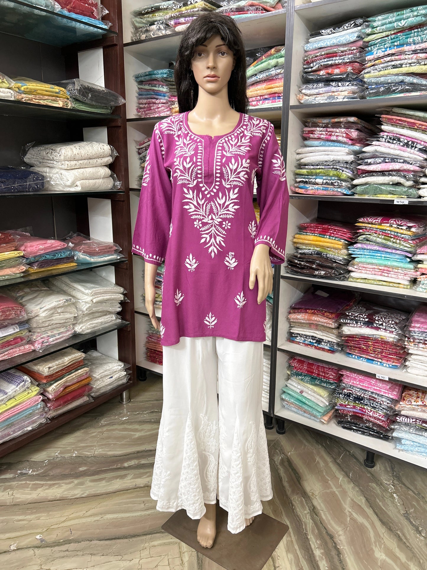 Mannequin wearing a purple embroidered top and white pants in a fabric store.