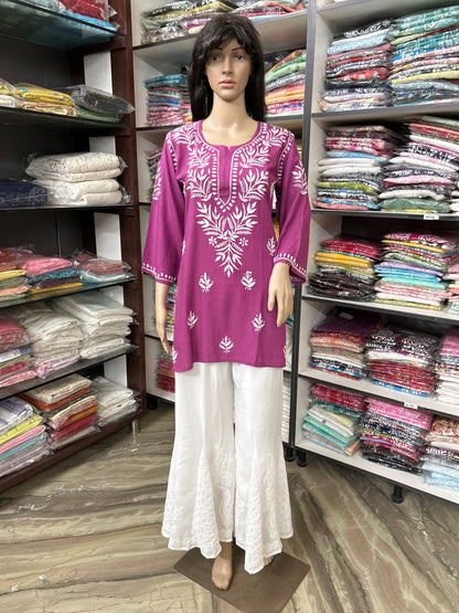 Mannequin wearing a purple embroidered top and white pants in a fabric store.