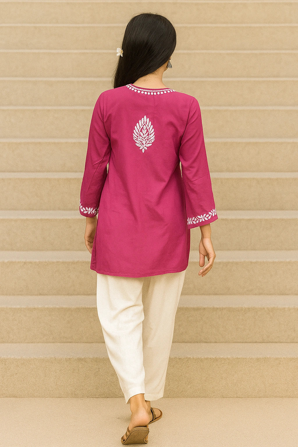 Person wearing a pink embroidered kurta with white pants on a beige staircase.