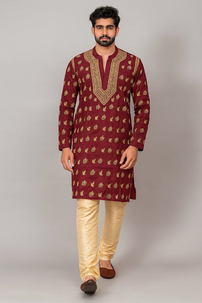 A man modeling a traditional Indian outfit consisting of a maroon kurta with gold embroidery and beige trousers, standing against a neutral gray studio background.