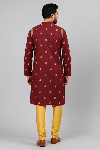 A man viewed from the back wearing a maroon long kurta with small gold motifs and mustard yellow trousers, standing against a light gray studio background.
