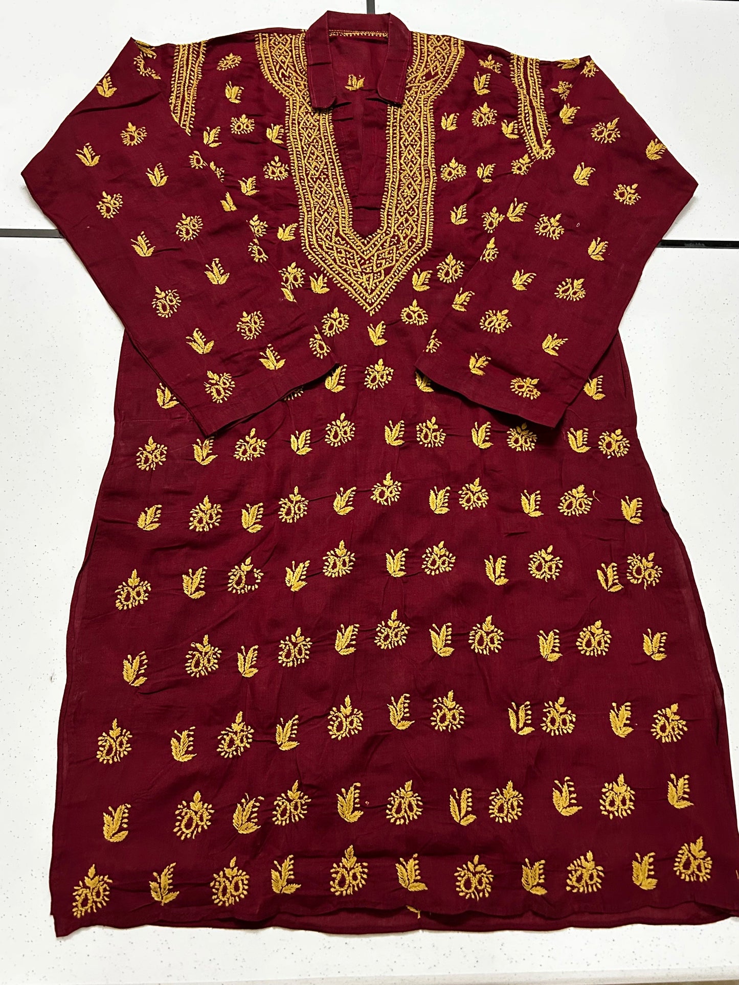 A maroon long kurta with gold floral and sunburst motifs, featuring a gold embroidered V-neckline and matching gold embroidery on the sleeves, laid flat against a white background.