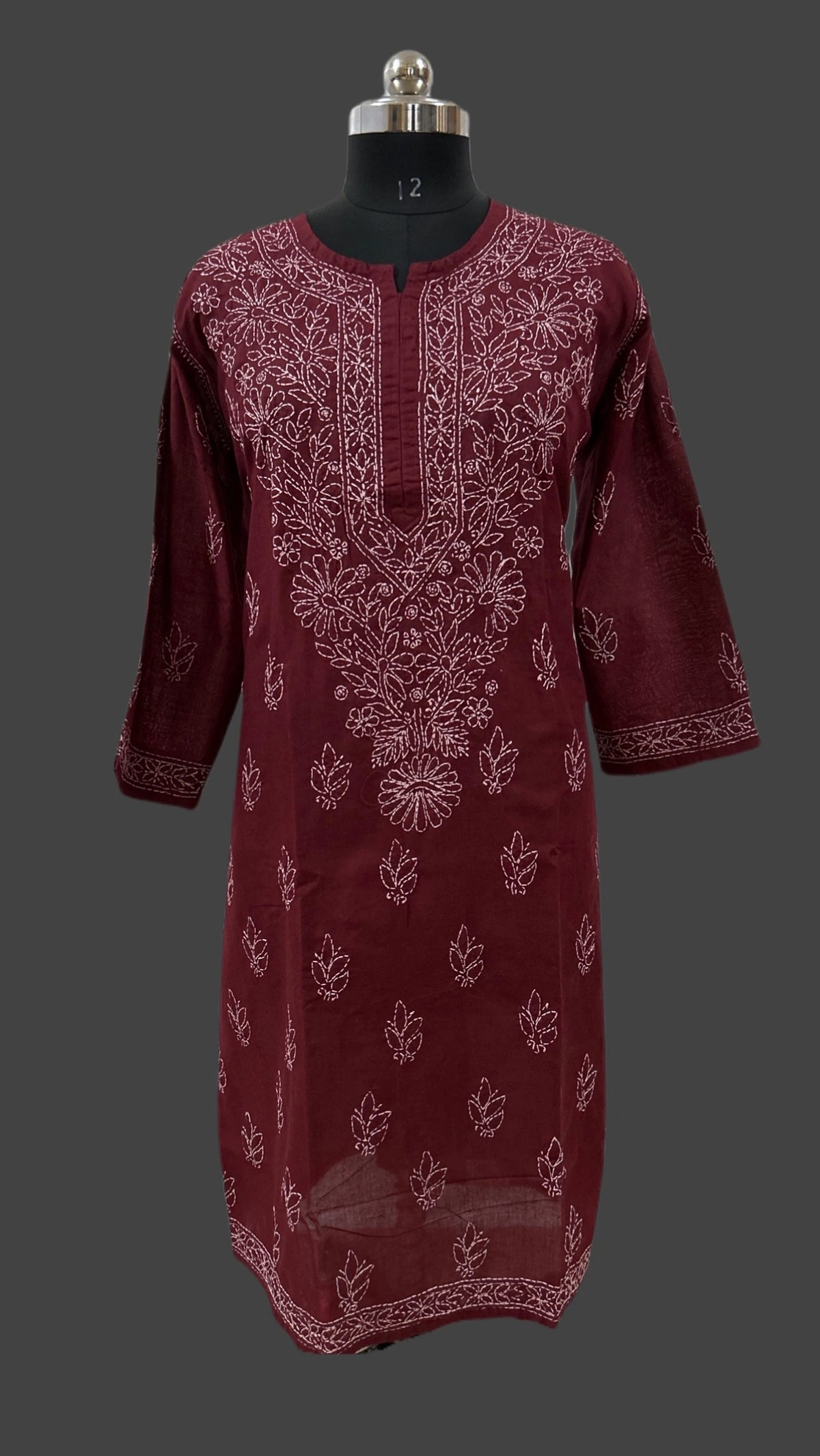 A maroon long kurta with white floral embroidery, displayed on a black dress form mannequin against a dark gray background.