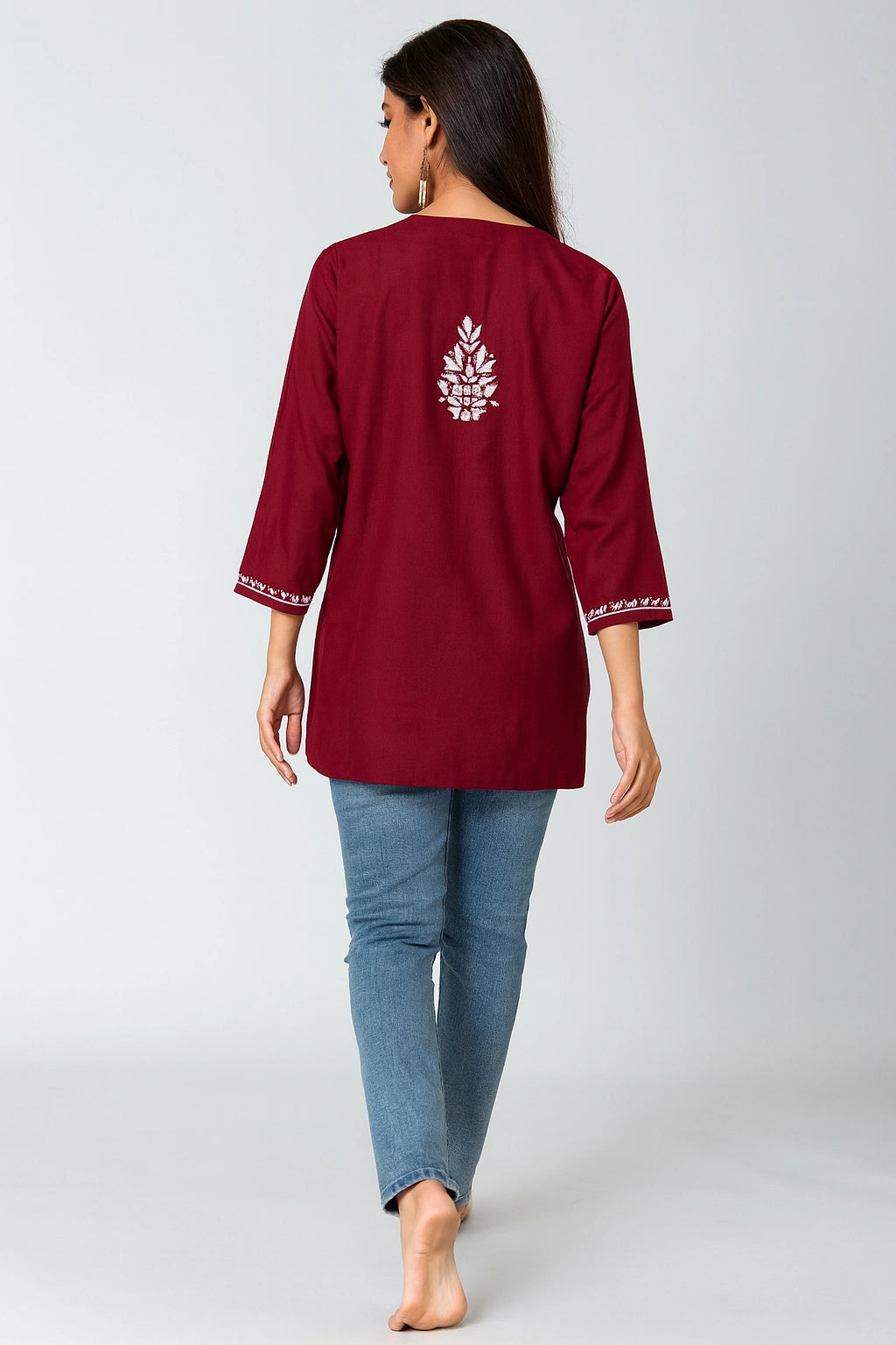 Woman wearing a maroon embroidered top and blue jeans on a white background