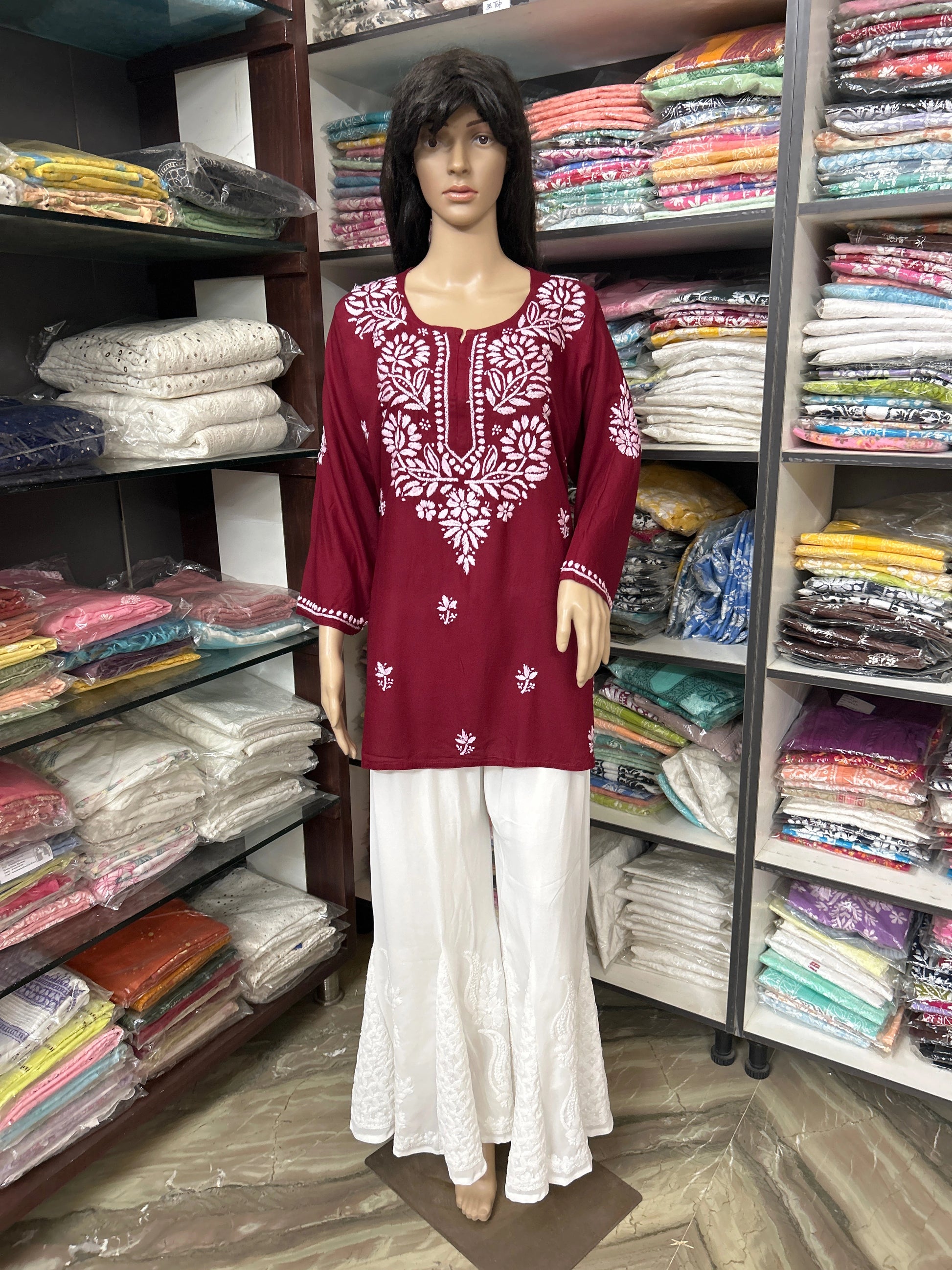Mannequin wearing a red embroidered top and white pants in a fabric store.