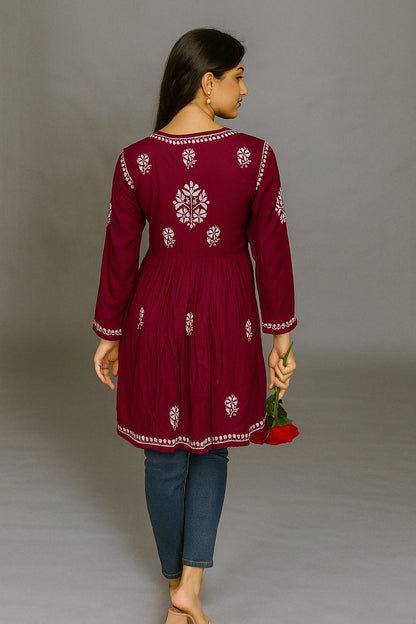 Woman wearing a maroon embroidered dress with blue jeans against a gray background