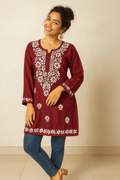 Woman wearing a maroon embroidered dress with white patterns on a beige background