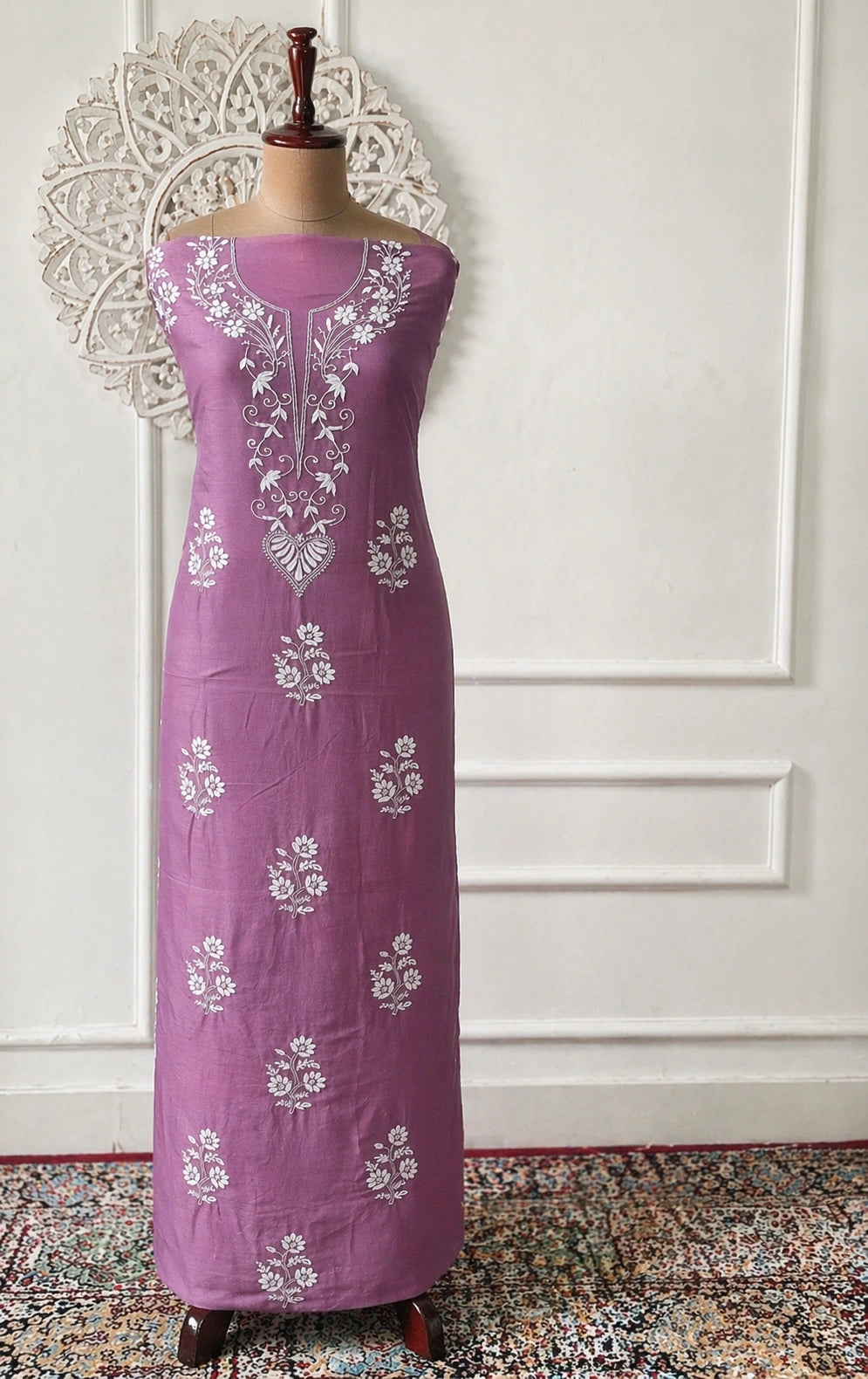 Purple dress with white floral embroidery on a mannequin against a white wall.