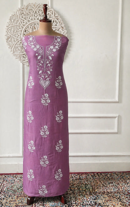 Purple dress with white floral embroidery on a mannequin against a white wall.