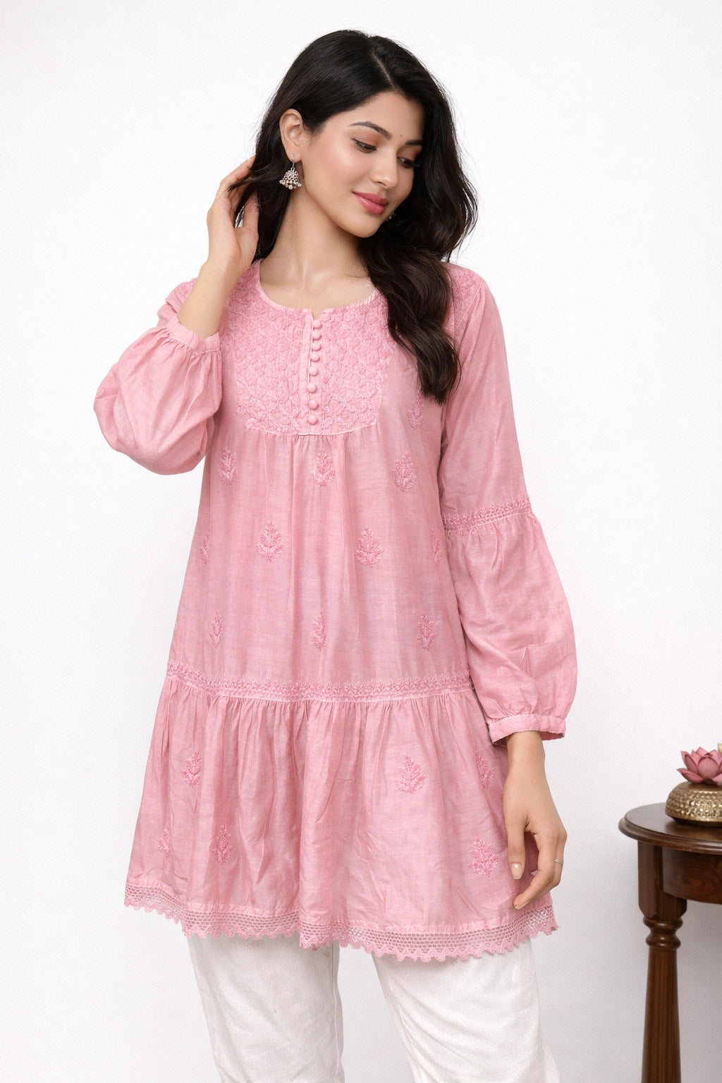 Woman wearing a lucknowi chikankari pink kurta with white pants on a white background
