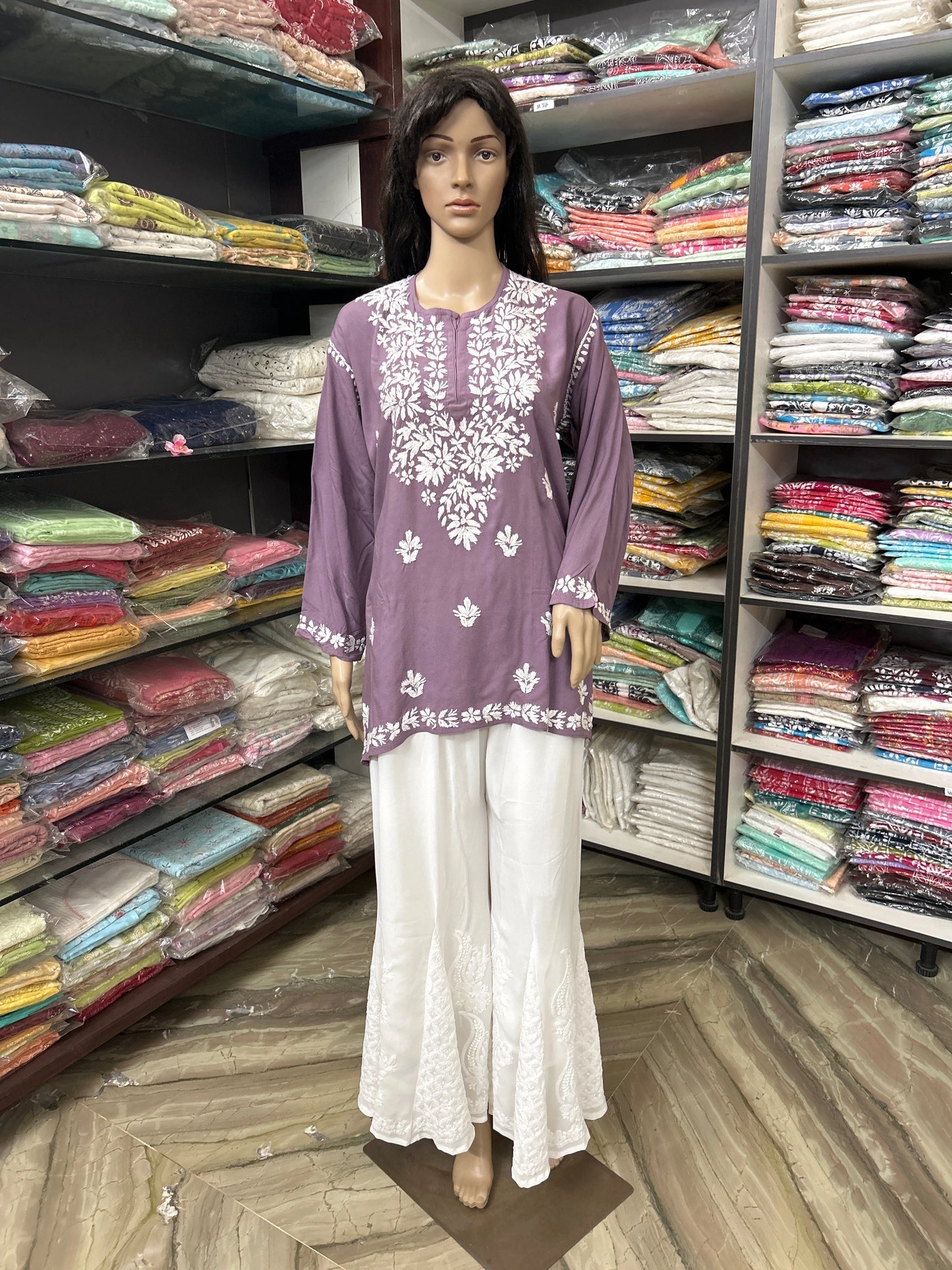 Mannequin wearing a purple embroidered top and white pants in a fabric store.