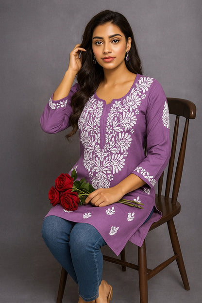 Woman wearing a purple embroidered top sitting on a chair with a gray background