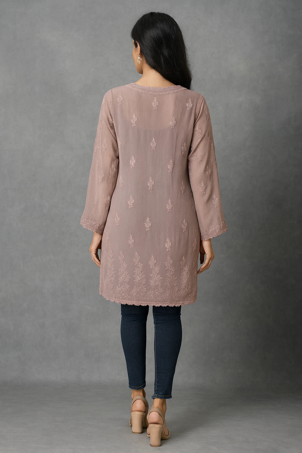 Woman wearing a pink embroidered kurta with blue jeans against a gray background