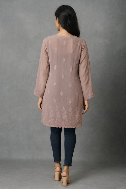Woman wearing a pink embroidered kurta with blue jeans against a gray background
