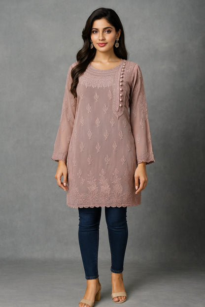 Woman wearing a mauve embroidered kurta with blue jeans against a gray background