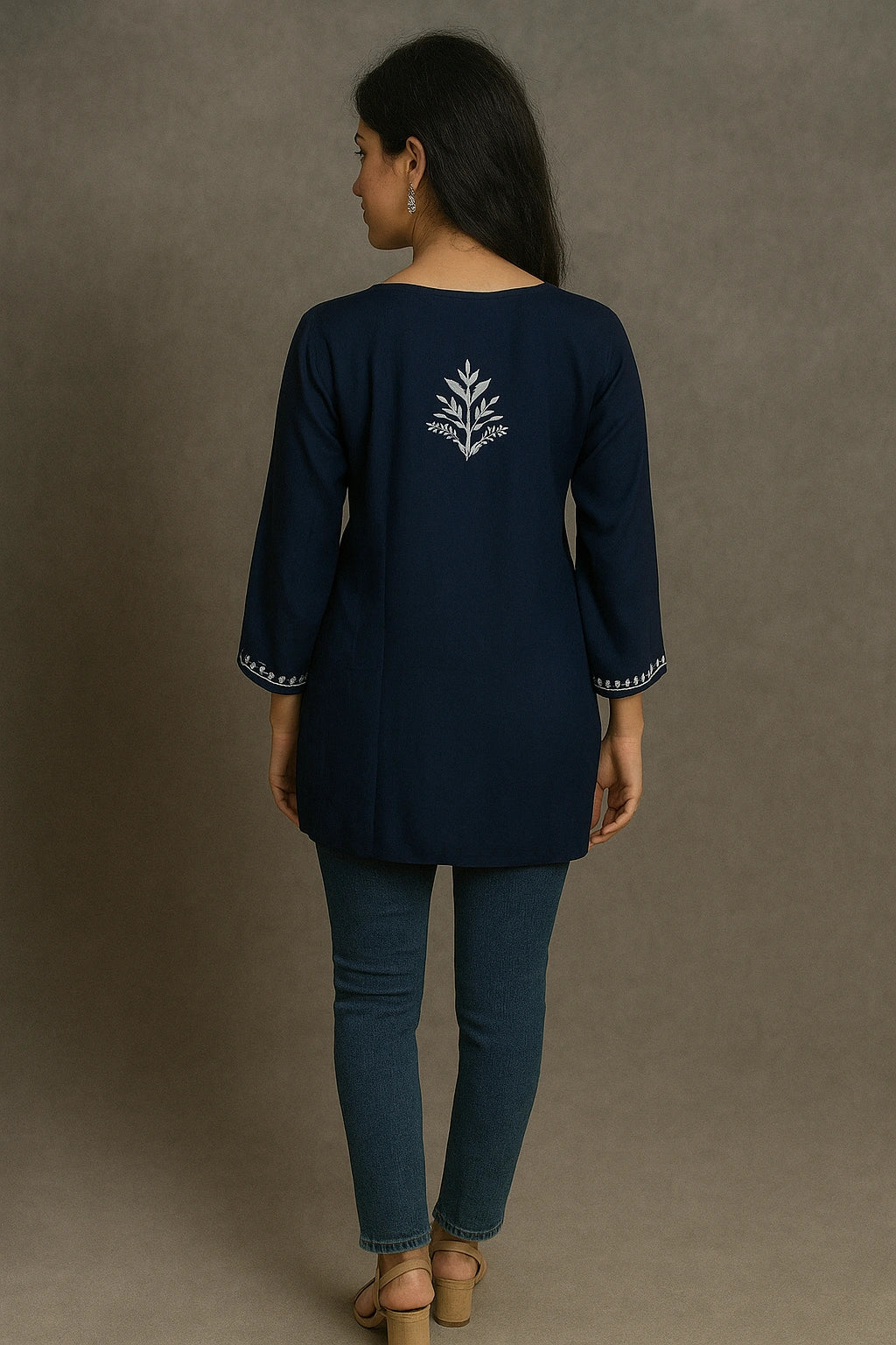Woman wearing a lucknowi chikankari navy blue top with a white design on the back, standing against a gray background.