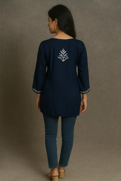 Woman wearing a lucknowi chikankari navy blue top with a white design on the back, standing against a gray background.