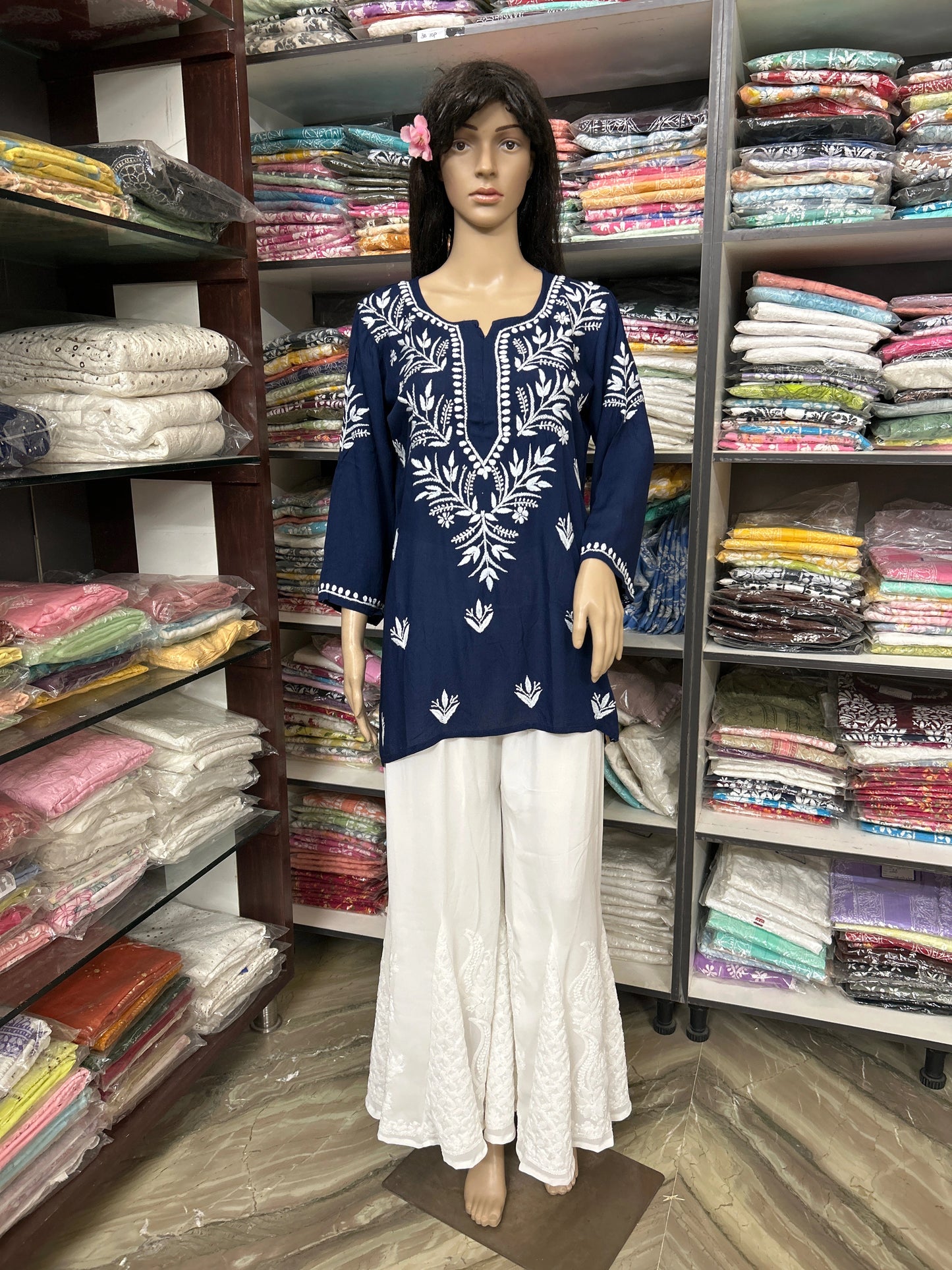 Mannequin wearing a blue embroidered top and white pants in a fabric store.