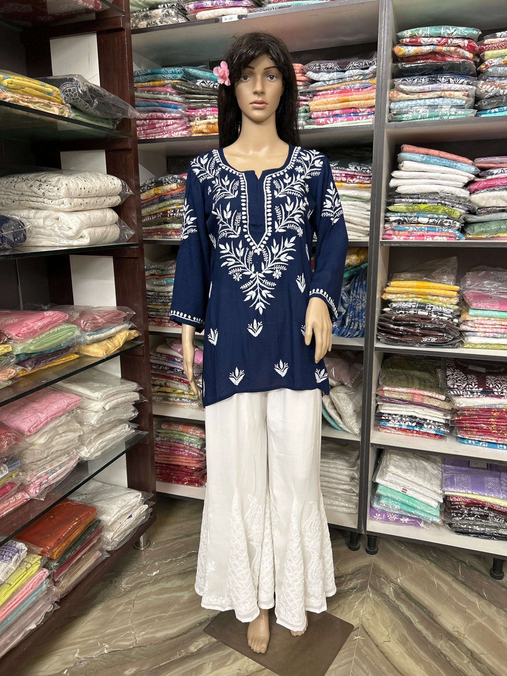 Mannequin wearing a blue embroidered top and white pants in a fabric store.