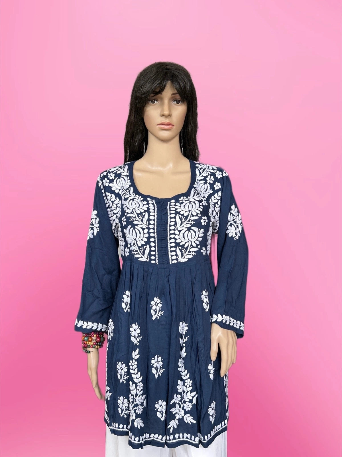 Woman wearing a lucknowi chikankari blue top with white polka dots and blue jeans on a gray background