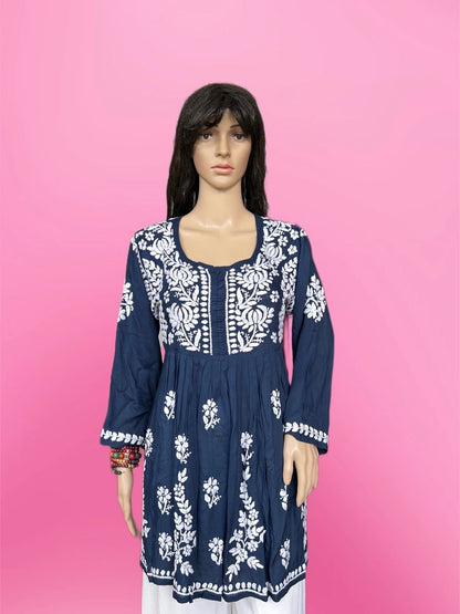 Woman wearing a lucknowi chikankari blue top with white polka dots and blue jeans on a gray background