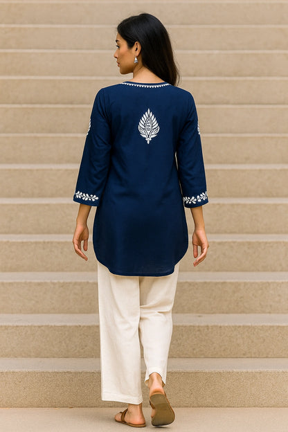 Woman wearing a lucknowi chikankari blue top with white polka dots and blue jeans on a gray background