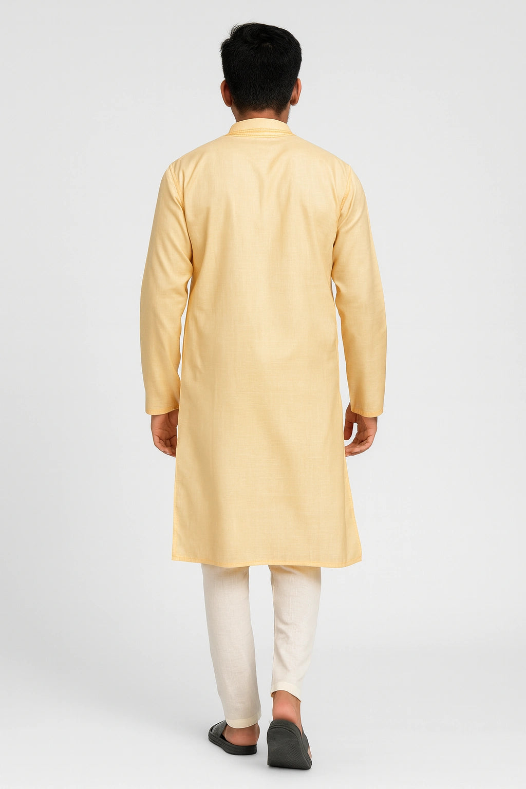 Man wearing a lucknowi chikankari yellow kurta with white pants on a light gray background