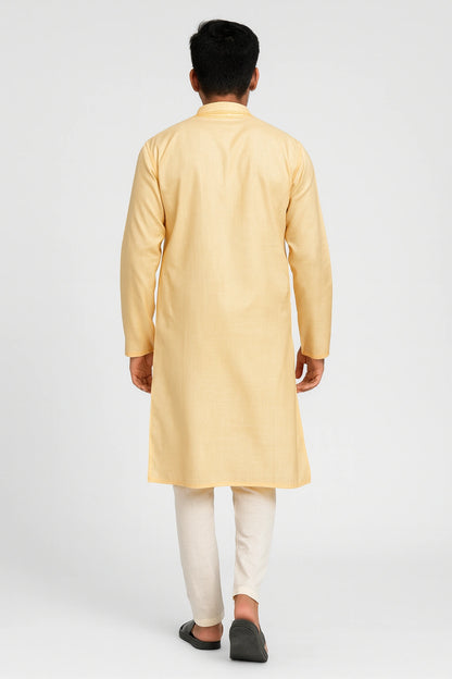 Man wearing a lucknowi chikankari yellow kurta with white pants on a light gray background