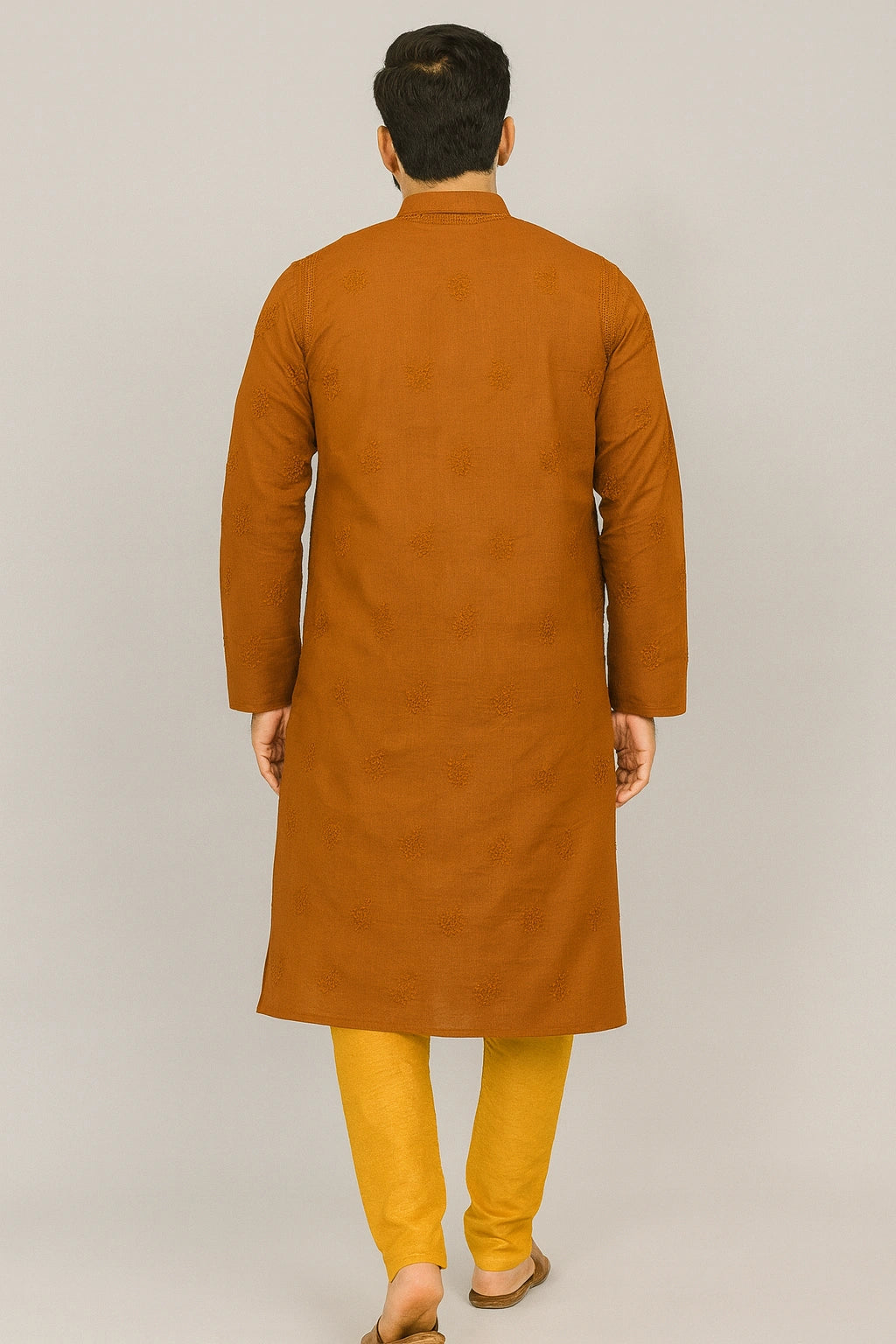 Lucknowi chikankari A man viewed from behind wearing a long-sleeved mustard-brown kurta paired with yellow trousers, standing against a plain light gray studio background.