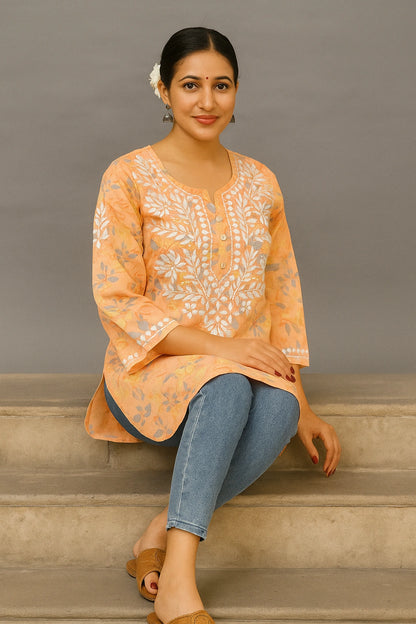 lucknowi chikankari Woman sitting on steps wearing an orange floral blouse and blue jeans against a gray background