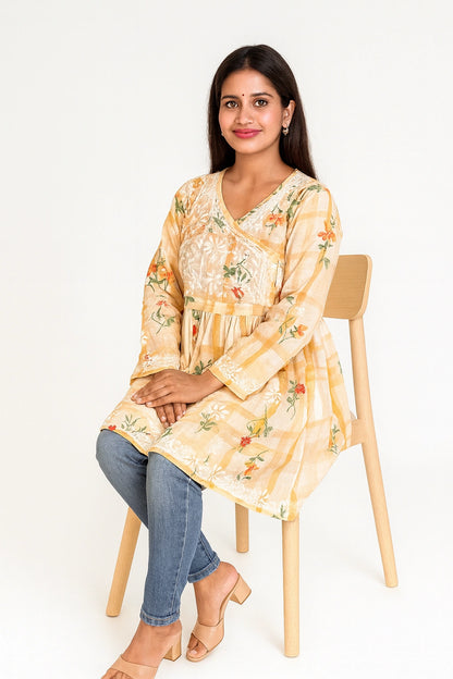 lucknowi chikankari Woman wearing a yellow floral dress sitting on a wooden chair against a white background