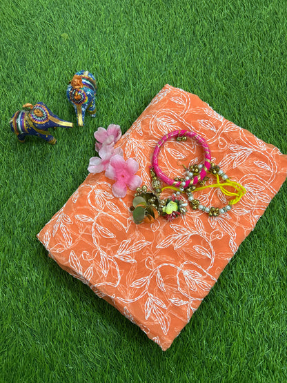 Lucknowi chikankari An orange tepchi work georgette dupatta, styled on green artificial grass with pink flowers, a pink bracelet, and two small decorative elephant figurines.