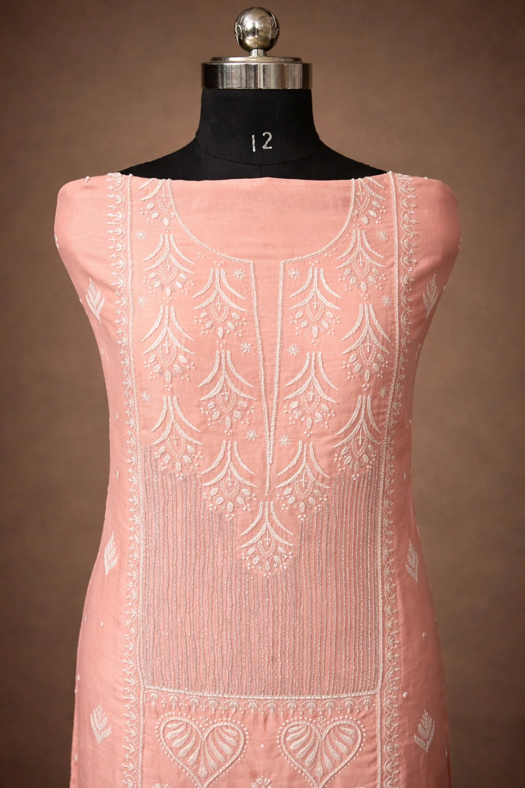 Pink sleeveless dress with intricate white embroidery on a mannequin against a brown background