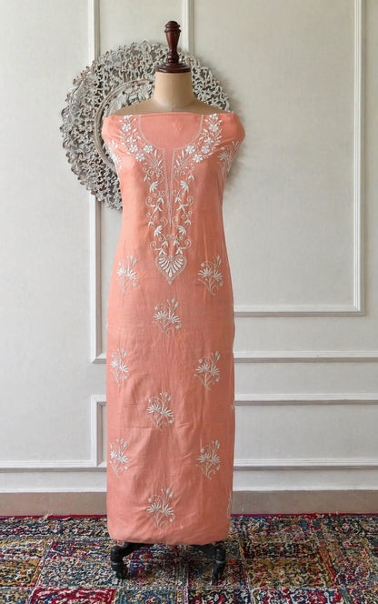 Peach-colored dress with floral embroidery on a mannequin against a white paneled wall.